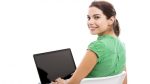 Kobieta w zielonej bluzce siedząca przy laptopie odchyla głowę
